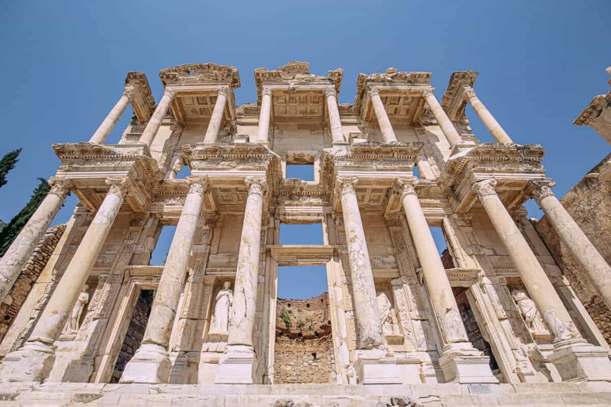 Imposing marble facade of the Celsus Library in Ephesus, with tall Corinthian columns and carved statues under a clear sky.