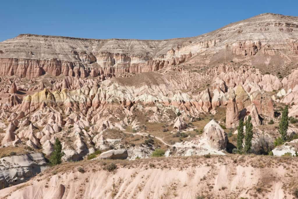 Eroded red rock formations in Cappadocia's Red Valley under soft daylight with rugged cliffs and unique terrain.