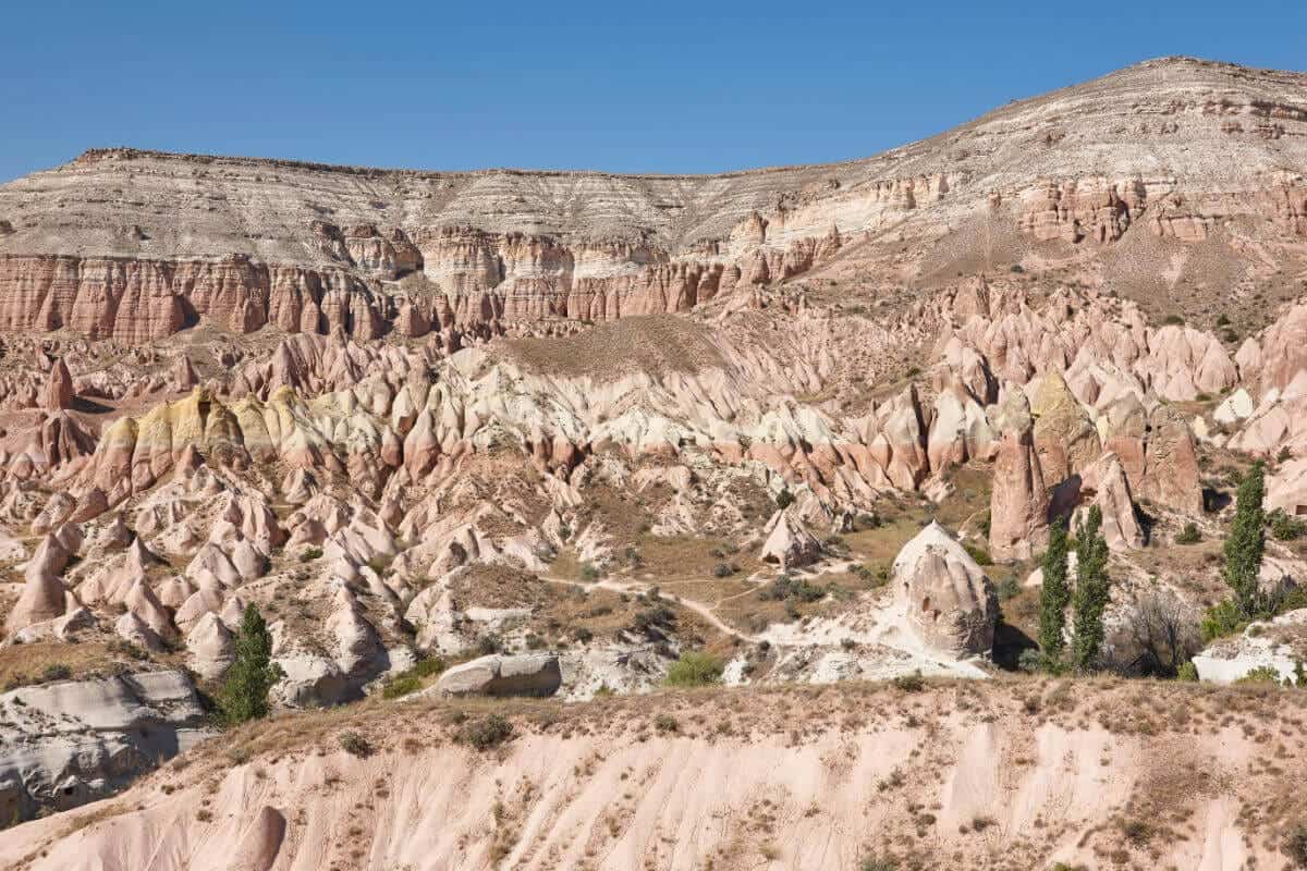 Eroded red rock formations in Cappadocia's Red Valley under soft daylight with rugged cliffs and unique terrain.