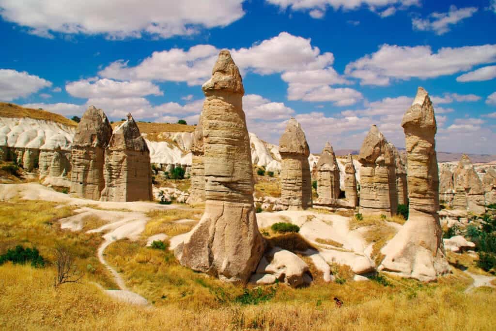 Tall, phallic-shaped fairy chimneys in Love Valley, Cappadocia, under a bright blue sky with scattered clouds.