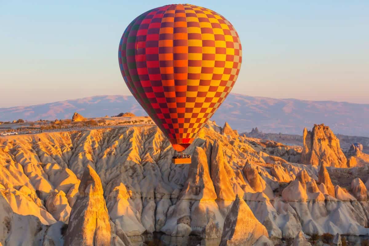 Colorful hot air balloon soaring above Cappadocia's rocky fairy chimneys at sunrise in Nevşehir, Turkey.