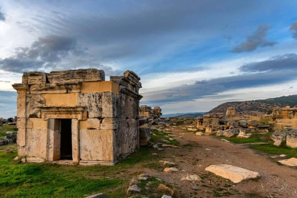 Ancient stone tomb structure in the necropolis of Hierapolis, Pamukkale, with dramatic skies and scattered ruins.