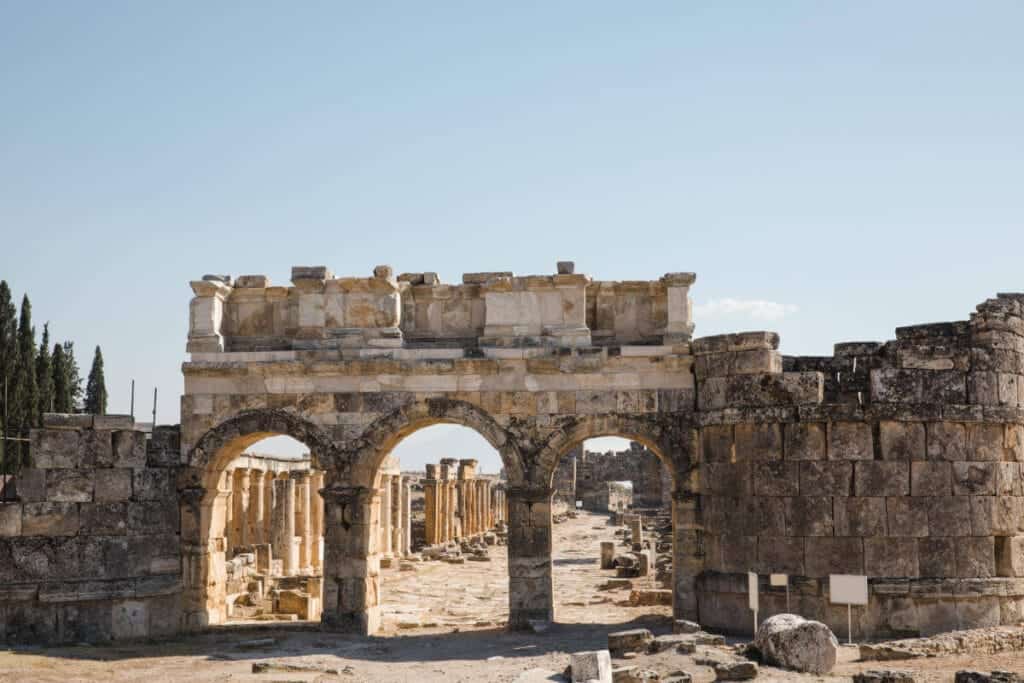 Ancient Roman gate with triple arch design in Hierapolis ruins, Pamukkale, Turkey under clear blue sky.