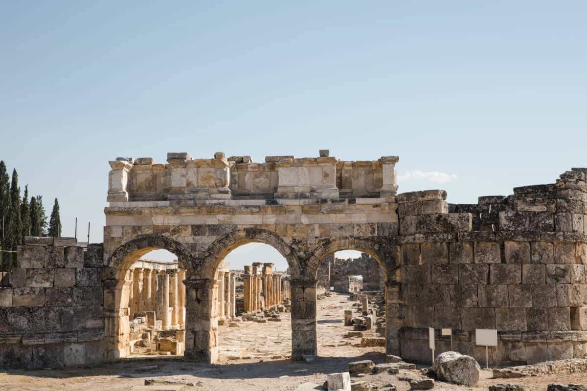Ancient Roman gate with triple arch design in Hierapolis ruins, Pamukkale, Turkey under clear blue sky.