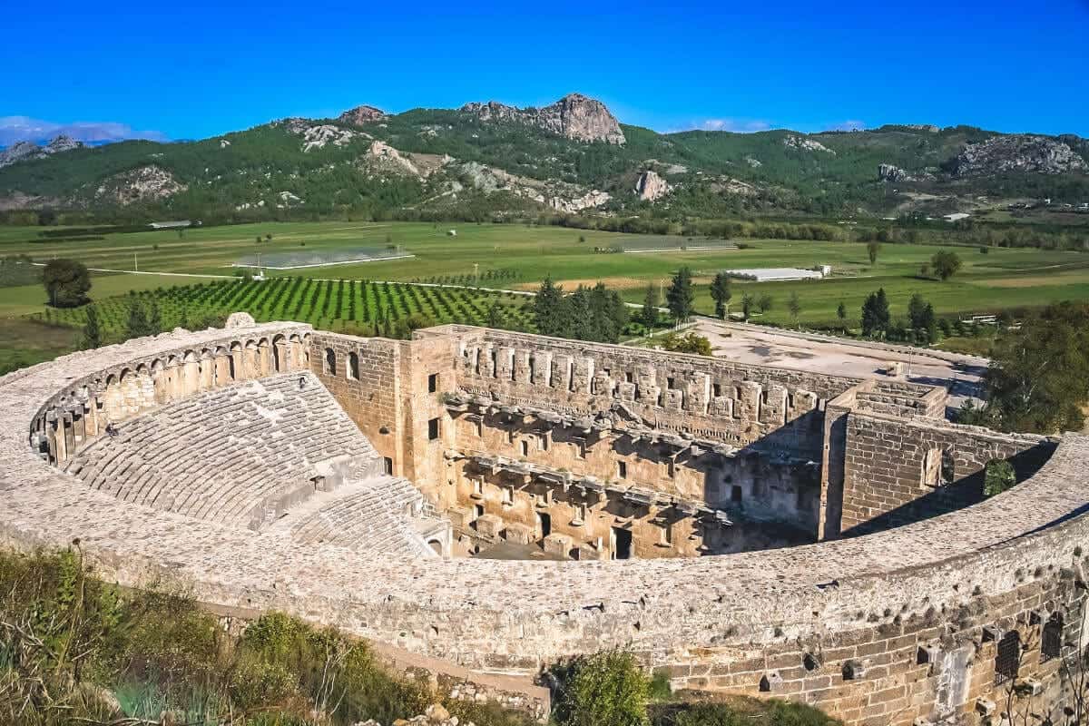 Well-preserved Roman Theatre of Aspendos in Antalya, Turkey, surrounded by green fields and distant mountains.