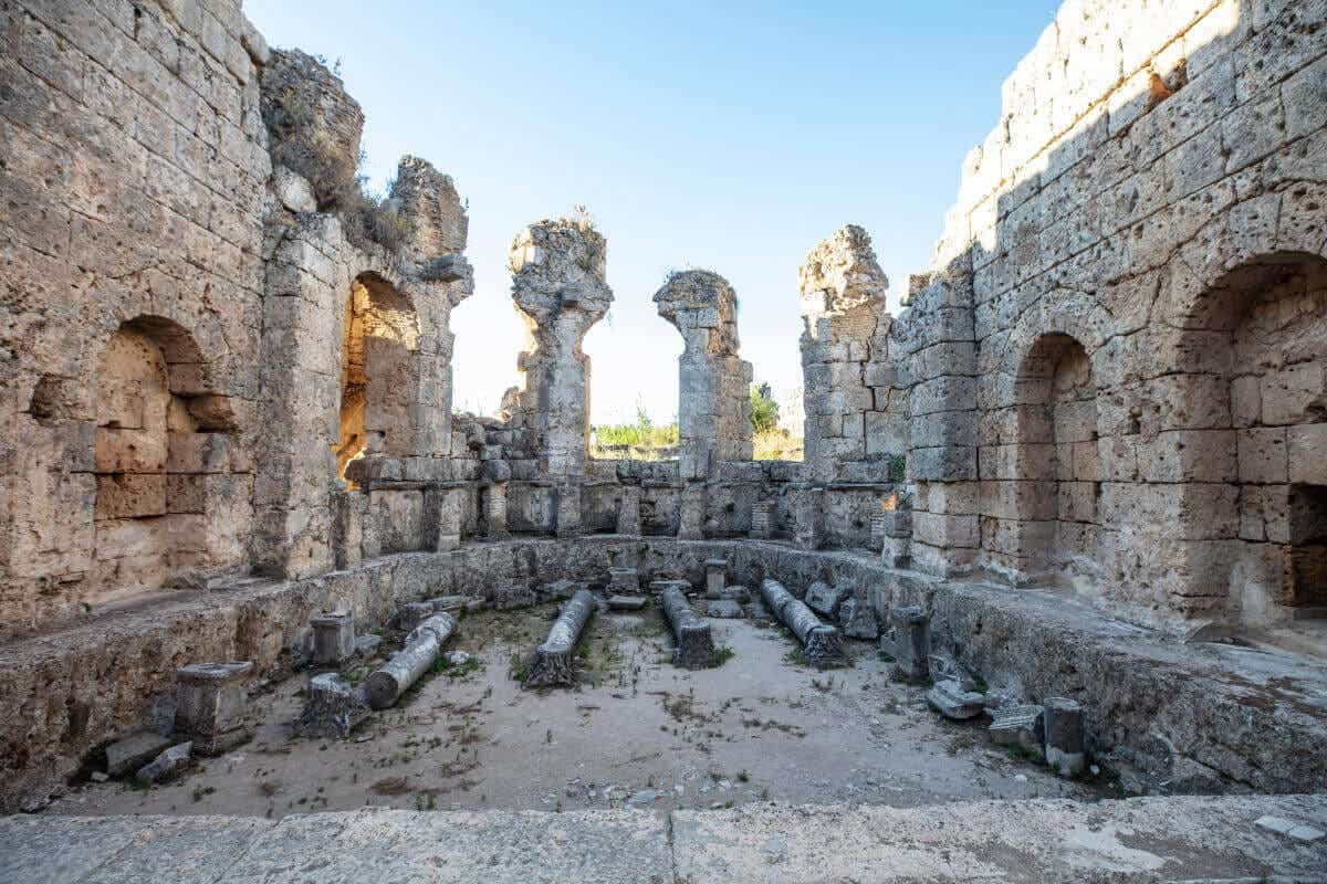 Ancient Roman bath ruins with arched niches and stone columns in Perge, Antalya, Turkey, illuminated by natural light.