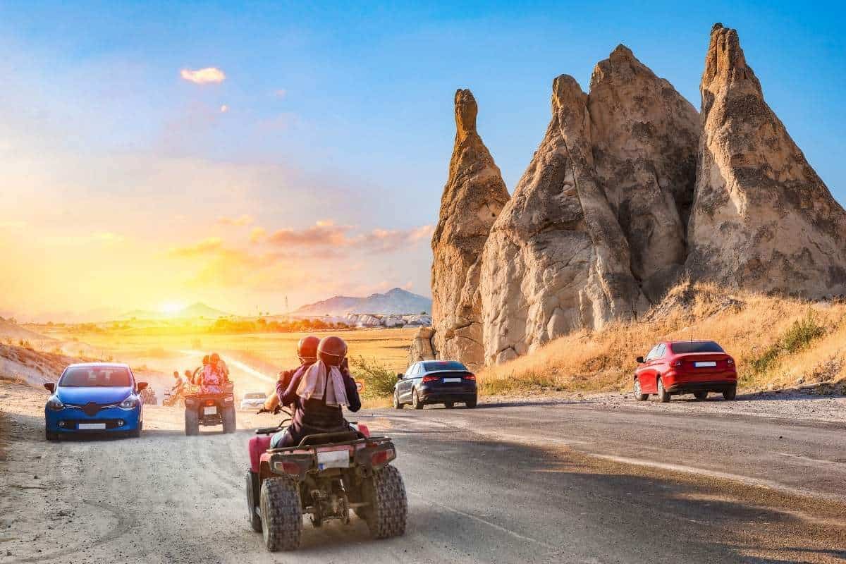 Travelers on ATVs ride past unique Cappadocia rock formations at sunset on a scenic adventure route.
