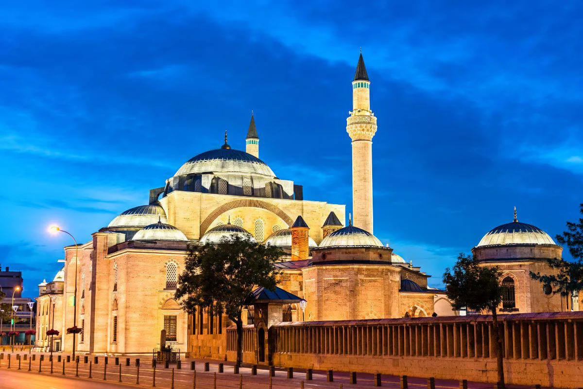 Illuminated Selimiye Mosque in Konya, Turkey at dusk with domes and minaret against a deep blue sky.