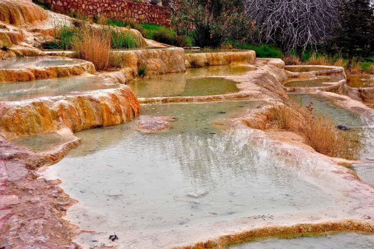 Iron-rich travertine terraces at Karahayit Red Springs with warm thermal pools and natural vegetation.