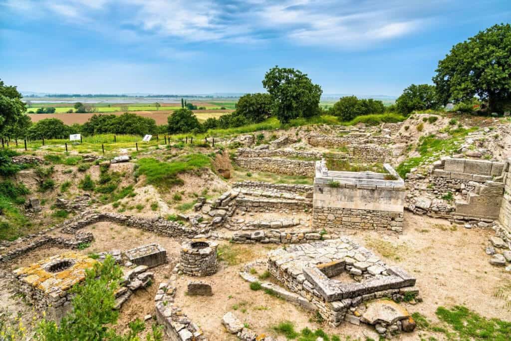 Stone walls and excavated ruins of ancient Troy in Çanakkale, surrounded by dry grass and open skies.