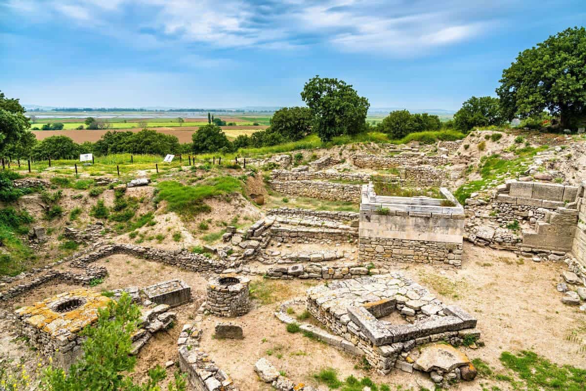 Stone walls and excavated ruins of ancient Troy in Çanakkale, surrounded by dry grass and open skies.