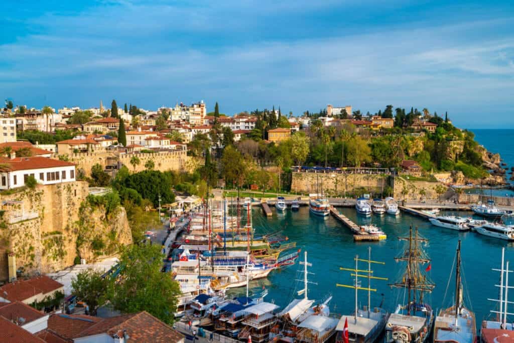 Boats docked in Antalya Kaleiçi Marina with historic Old Town houses and ancient stone walls in the background.