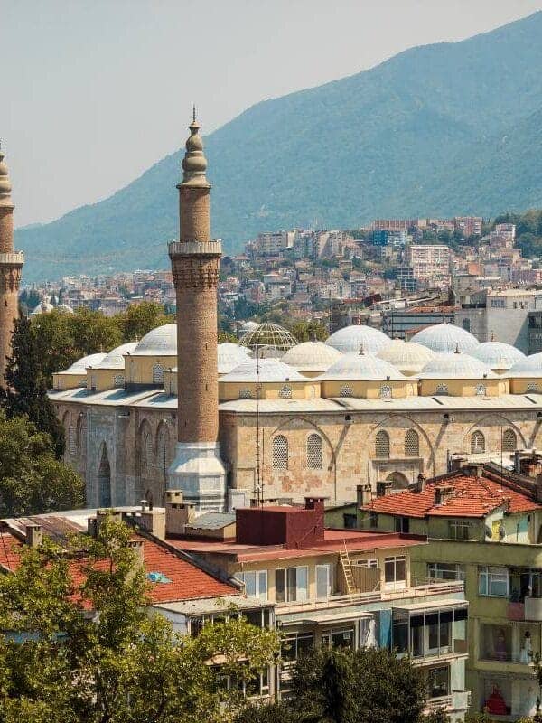 Ulu Cami mosque with twin minarets surrounded by Bursa city buildings and green mountain backdrop
