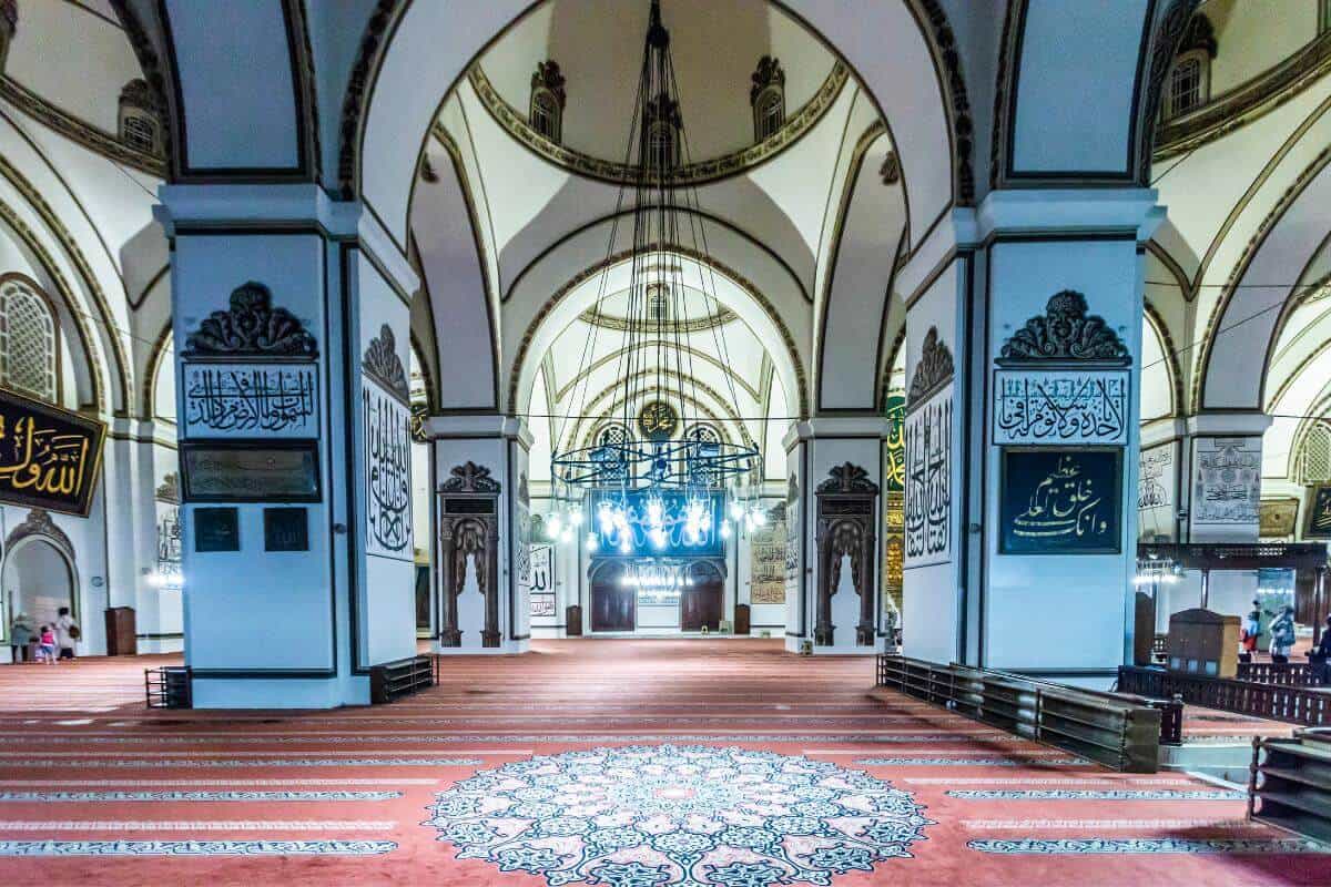 Ornate interior of Ulu Cami in Bursa featuring Islamic calligraphy, arched ceilings, and elegant chandeliers