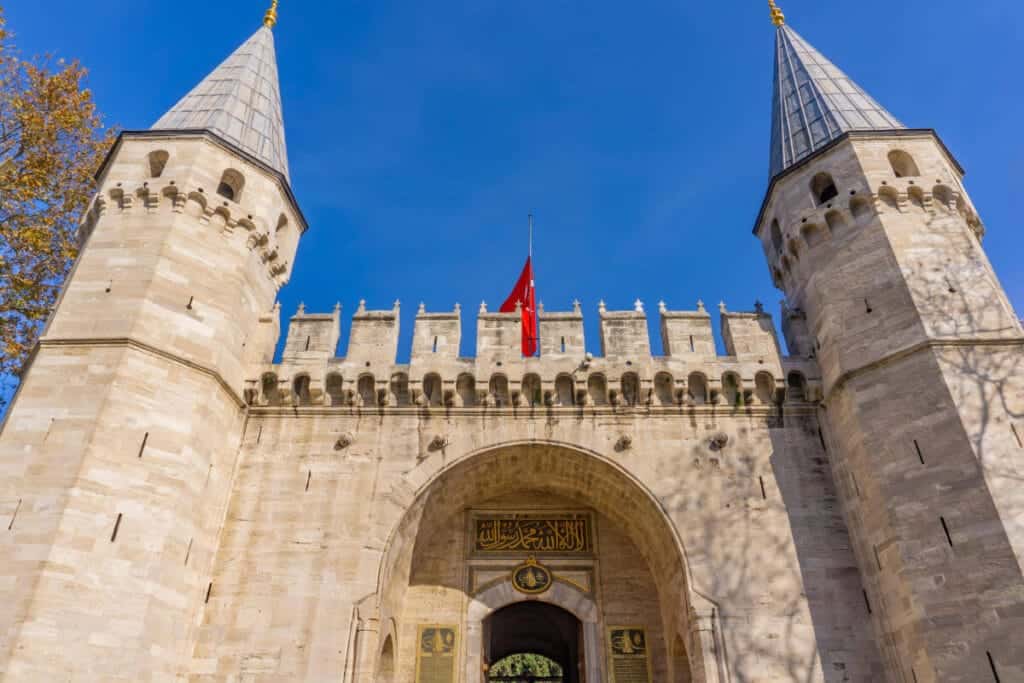 Historic main gate of Topkapi Palace in Istanbul with twin towers and Ottoman architectural design under blue sky.