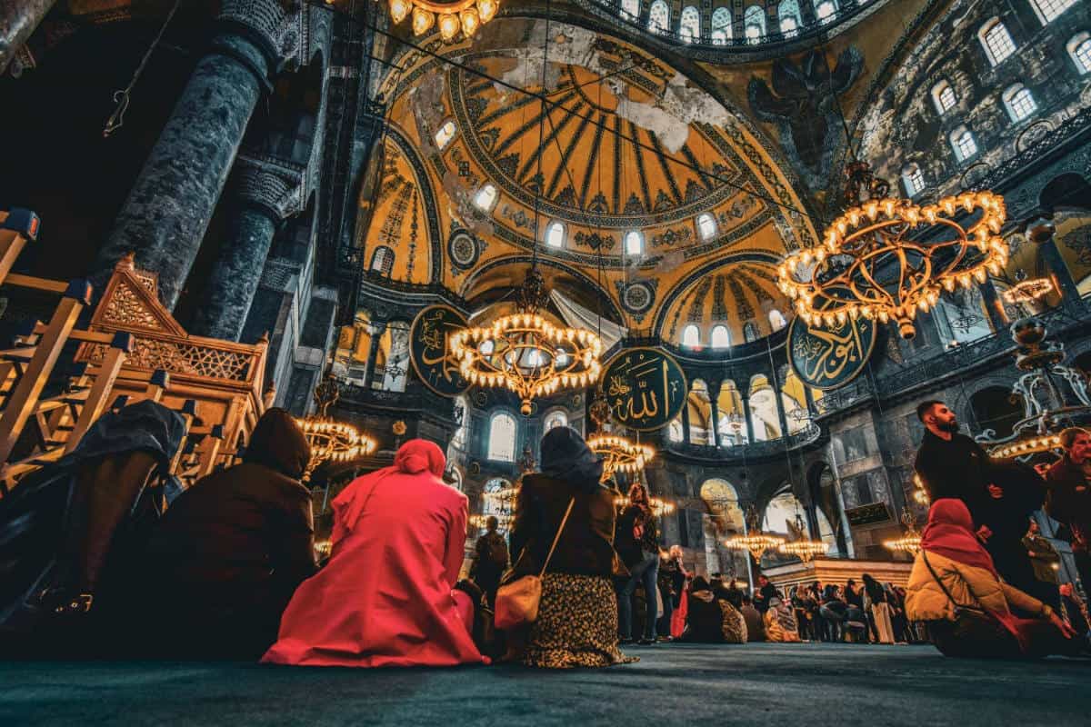 Interior of Hagia Sophia with worshippers beneath grand domes and chandeliers in historic Istanbul setting.