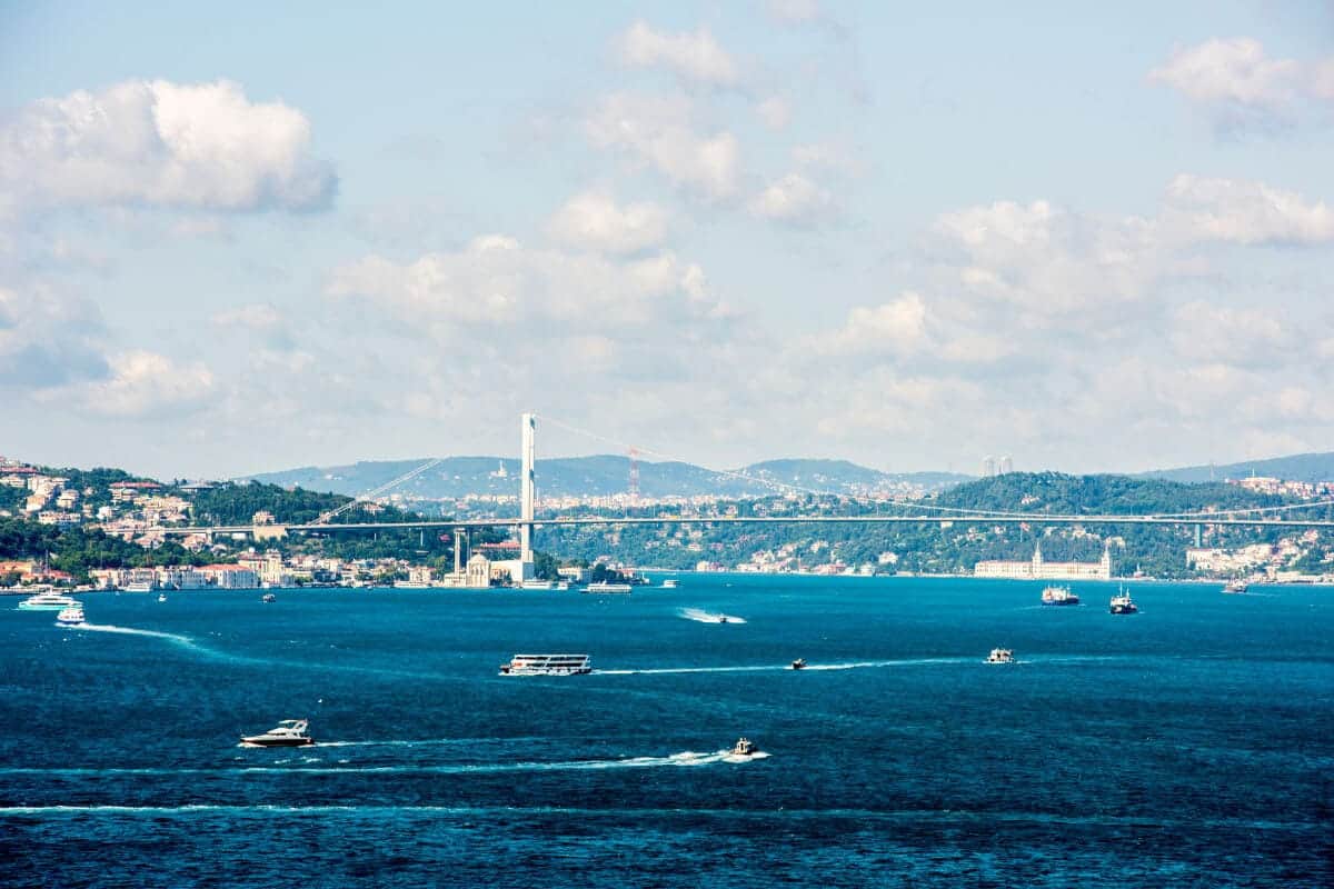 Expansive view of Istanbul's Bosphorus Strait featuring bustling boats, scenic hills, and the iconic Bosphorus Bridge on a partly cloudy day.