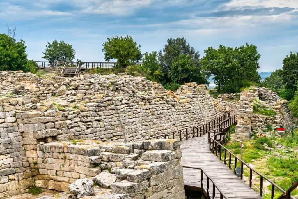 Stone seating and wooden stage of the ancient theater in the archaeological site of Troy, surrounded by trees
