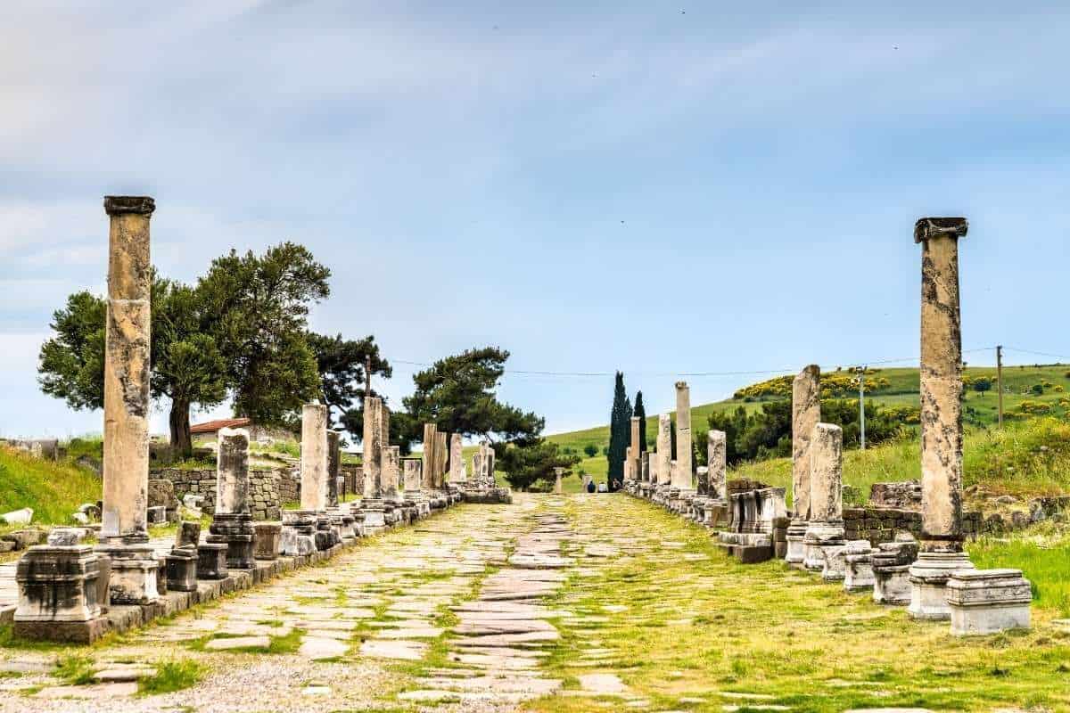Ancient colonnaded Sacred Way street at the Asklepieion of Pergamon ruins in Bergama, Turkey, under a blue sky.