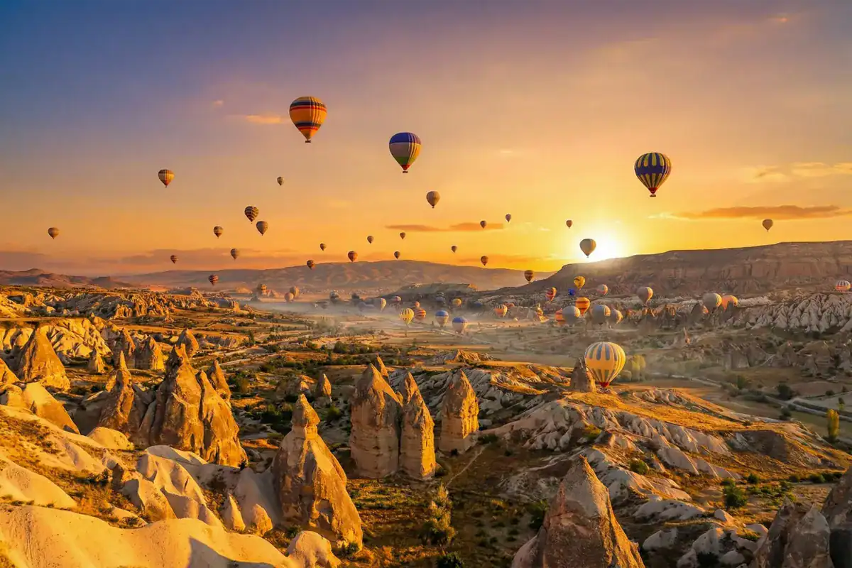 Hot air balloons flying at golden sunrise over the unique rock formations and fairy chimneys of Cappadocia, Turkey. A highlight of the Best of Turkey tour.