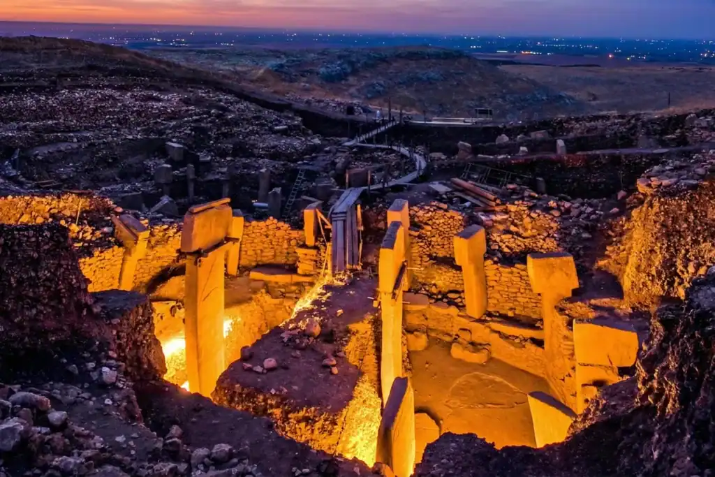 Ancient Göbekli Tepe archaeological site illuminated at dusk, showcasing its massive stone pillars a.