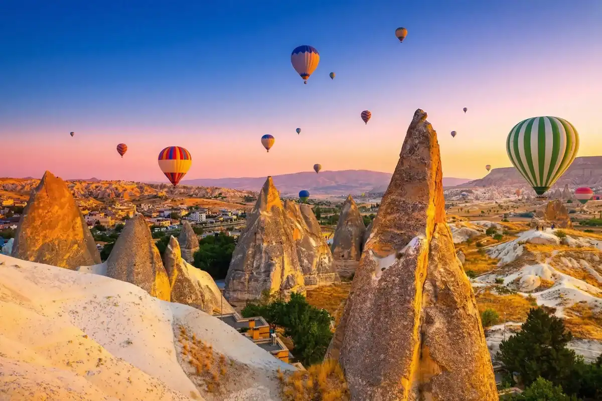 Dozens of vibrant hot air balloons floating gracefully over the illuminated, golden fairy chimneys of Cappadocia at sunrise, as One Nation Travel guides guests on a breathtaking aerial tour of the historic Turkish landscape.