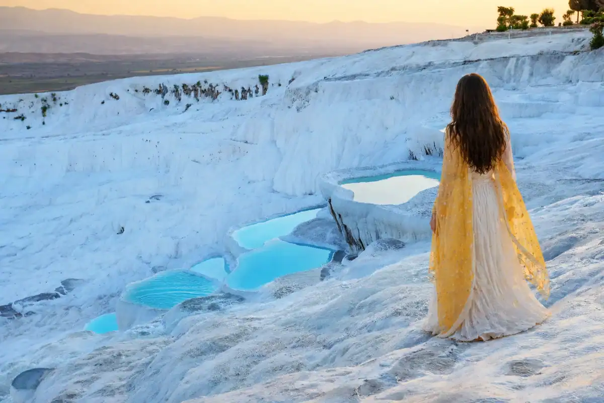 Woman overlooking Pamukkale travertine terraces and turquoise thermal pools at sunset, Turkey